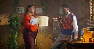 A man and a woman are talking standing in a retro office. A man is drinking coffee. A woman holds documents in her hands photo