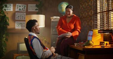 A man and a woman are talking sitting in a retro office. A woman is sitting on a table photo