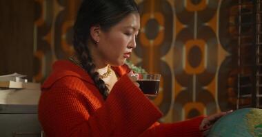 The woman turns the globe thoughtfully and drinks coffee. Retro office worker photo