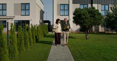 A husband and wife are looking at a booklet with a design project of a house while walking in the backyard photo