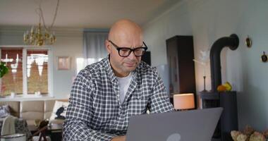 The man works from home. He uses a laptop and writes in a notebook with serious look photo