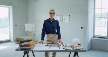 Portrait of the designer in a room without decoration. She smiles at the camera as she stands next to a table with documents and paint samples photo