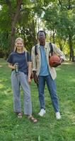 A young man and a woman smile at the camera while standing in a city park. A man holds a basketball in his hands. Students. Summer day photo