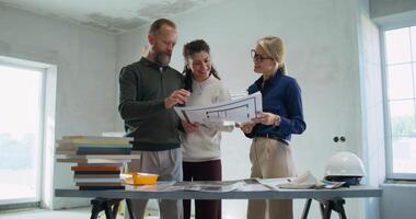 Happy customers discuss the design project of the house with the designer standing in a room without decoration photo
