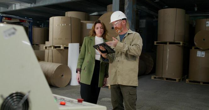 A worker and a boss talk and use a tablet while standing in the workshop at a paper mill. photo