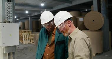 Two men in protective helmets and glasses are talking standing in a paper mill photo