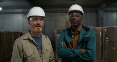 Two men in hard hats and work clothes are smiling at the camera. They are in the warehouse of a paper mill photo