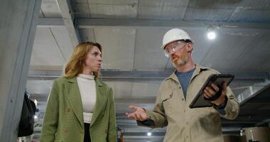 An employee and a woman in informal clothes are talking walking through the production hall of the factory with a serious look. A man holds a tablet in his hand photo