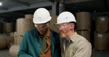 Two men in protective helmets and glasses are talking standing in a paper mill with a serious look photo