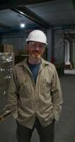 A man in a work uniform is smiling at the camera. He is in the factory warehouse photo