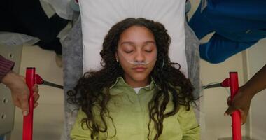 A woman with a breathing tube in her nose is lying on a gurney, top view. She is being driven down the hospital corridor, her eyes are closed photo
