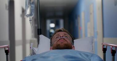 A man with an oxygen tube in his nose is lying on a medical cart. He is being driven along the hospital corridor photo