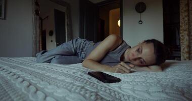 A woman is crying lying on a bed at home. Her mascara was leaking. The mobile phone is on the bed next to her photo