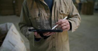 A man in a protective helmet and glasses uses a tablet while working at a factory. He uses a stylus photo