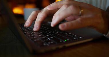 A man typing on a laptop while sitting at a desk at night. Close-up of his hands, unrecognizable persona photo