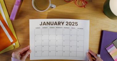 A woman puts a calendar sheet on the table, close-up of her hands, an unrecognizable person. Top view of the workplace photo
