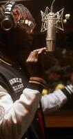 The rapper is recording a song in a recording studio. The sound engineer is sitting in the control room behind the glass photo