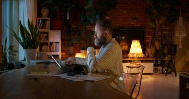A respectable man with a beard typing on a laptop while sitting at a desk at home. Night work. Remote workplace photo