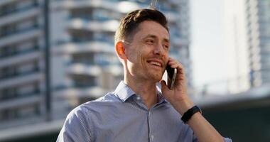 A man is talking on a mobile phone while standing in the business center of the city. Close-up of his smiling face photo
