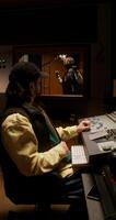 The sound engineer controls the recording process of the song in the studio. The rapper sings in the room behind the glass photo