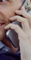 A happy man is talking on his mobile phone while standing outdoors. Close-up of his face photo