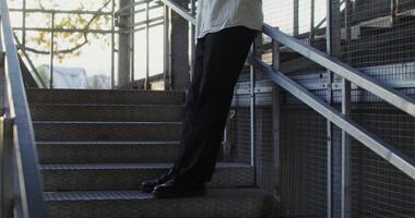 A young man of European appearance in a knitted hat uses a mobile phone, and drinks coffee while standing on the steps of a metal staircase photo
