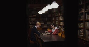 Young man and woman of European appearance start a chess game, thinking intently, sitting opposite each other at a table in the library photo