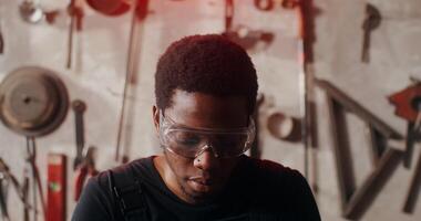 A man wearing glasses and a black shirt in front of a wall of tools photo