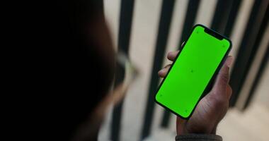 A mobile phone with a green screen in the hand of a man of African American appearance, filming from behind, his face is not visible. Copy space, mockup, chroma key. in 4k, red komodo photo