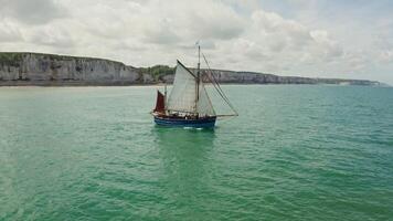 The sailing ship moves from the land, with picturesque sheer cliffs along the coast, towards the open sea. Drone , Etretat, France photo