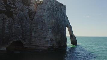 The drone flies through one of the natural arches, revealing a view of the mysterious beach at the foot of sheer cliffs. Etretat, France photo