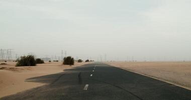 Asphalt road in the middle of the desert. The wind blows sand, covering the surface of the road. Power lines in the background. 4k , red komodo photo