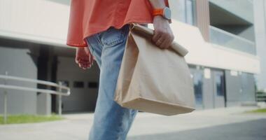 A man carries a paper bag with ready-made food walking around the city, close-up of his hands, no face photo