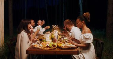 Guests smile and talk while eating sitting at a festive table outdoors at night photo