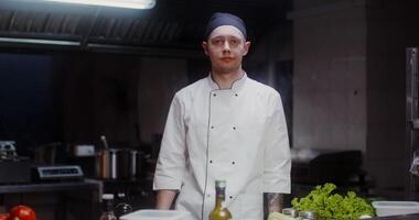 A man in a chef's uniform with a headband smiles while looking at the camera in a well-equipped restaurant kitchen photo