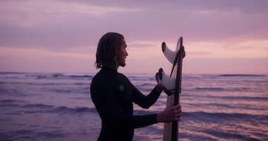 A man in a wetsuit holding a surfboard at sunset photo
