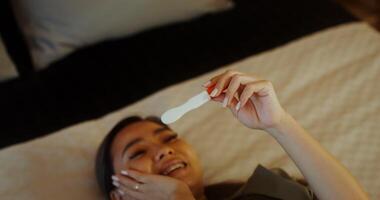 A woman is happy considering a positive pregnancy test in her hands while lying on the bed in the bedroom photo
