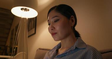 A woman is smiling typing on a laptop sitting on the couch in an apartment in the evening, close-up of her face photo