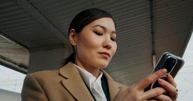 A woman in formal clothes and a coat uses a mobile phone standing on the platform of a railway station, close-up of her face photo