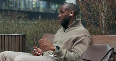 A man with earphones is talking on a mobile phone while sitting on a bench in the city. He's smiling. photo