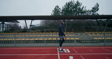 A man in sports clothes and with earphones walks through the stadium, resting after running on a cold day alone photo