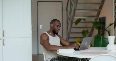 A man is smiling typing on a laptop and writing in a notebook while sitting at a table at home photo