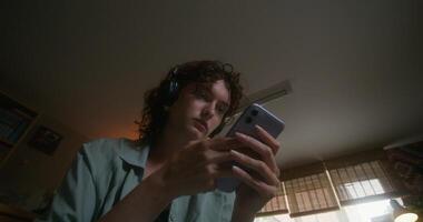 A young woman with headphones uses a mobile phone sitting on a bed at home with a sad look photo