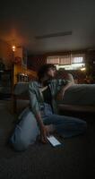 A young woman texting messages on a mobile phone while sitting on the floor near the bed with a depressed look photo