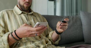 A man enters credit card details into a mobile phone for online purchases while sitting on the couch at home. Close-up of his hands, an unrecognizable person photo
