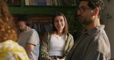 Young people in casual clothes smile and talk while sitting at a table indoors. Daylight photo