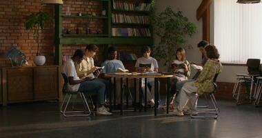 Group of young people of different nationalities are reading the Bible together while sitting at a table indoors. A woman reads aloud photo