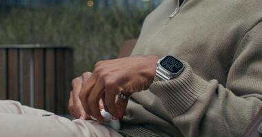 The man in the sweater takes the headphones out of the case and puts them on. He talks sitting on an outdoor bench with a serious look photo