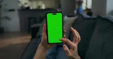 A woman uses a mobile phone with green screen lying on the couch at home, close-up of her hands, an unrecognizable person photo