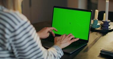 A woman uses a laptop with green screen sitting at a table at home, close-up of her hands, an unrecognizable person photo